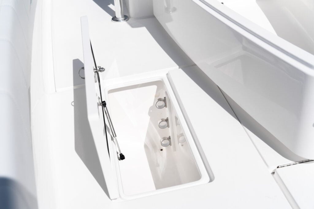 Open white hatch on a boat deck, revealing a clean and empty storage compartment with several socket holes.