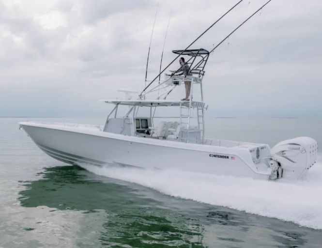 A white Contender boat cruising on calm water under a cloudy sky, equipped with multiple fishing rods and powered by twin outboard engines.